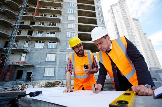 Entrepreneur général en compagnie d'un ingénieur civil, ils regardent les plans d'un chantier en cours derrière eux