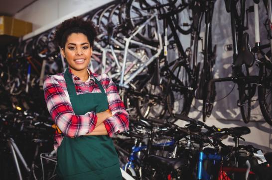 Jeune femme cheffe d'un magasin de vélos qui pose devant des vélos rangés verticalement
